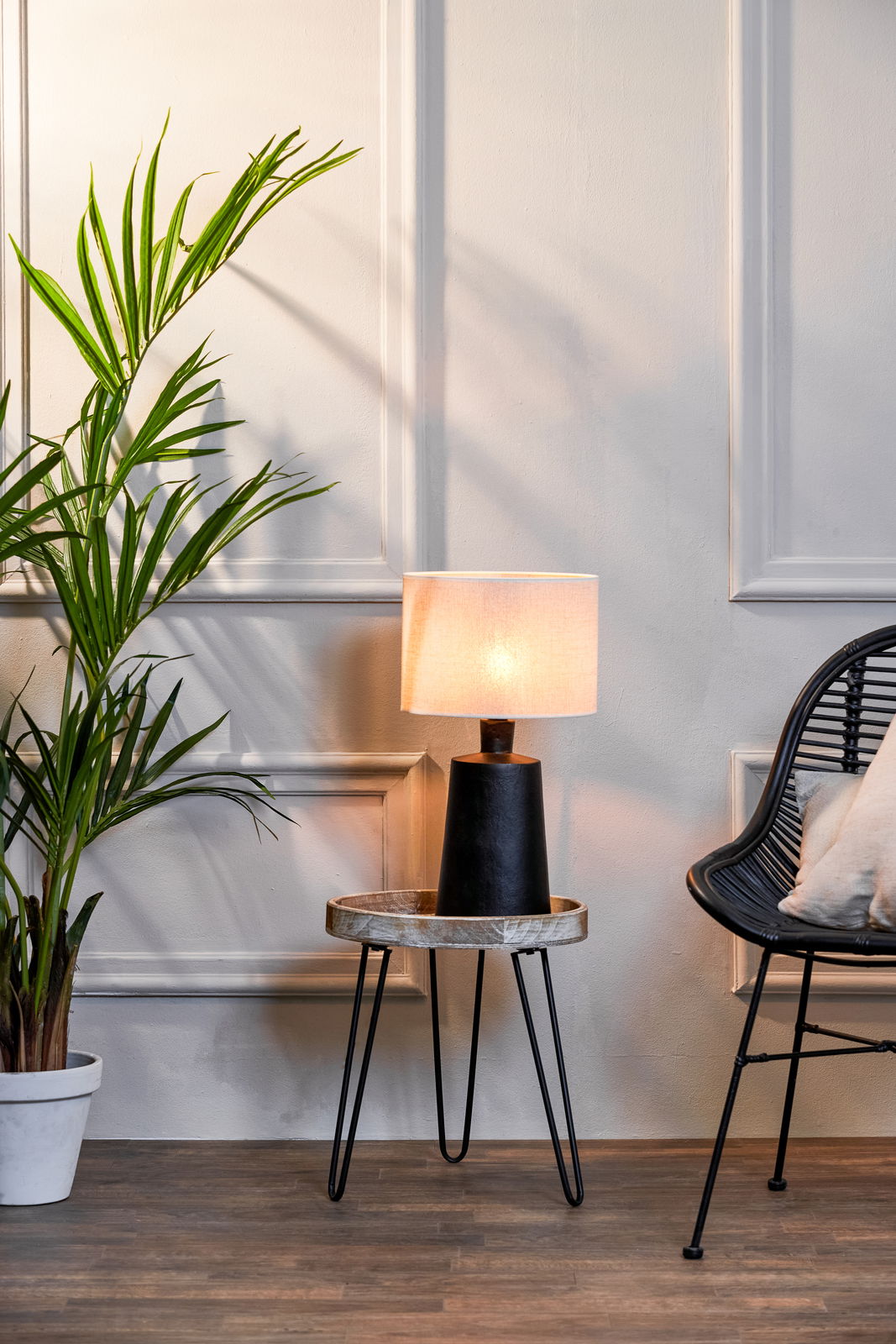 Moderner Lampenschirm auf einem kleinen Tisch, seitliche Perspektive, neben einer Pflanze und einem Stuhl.