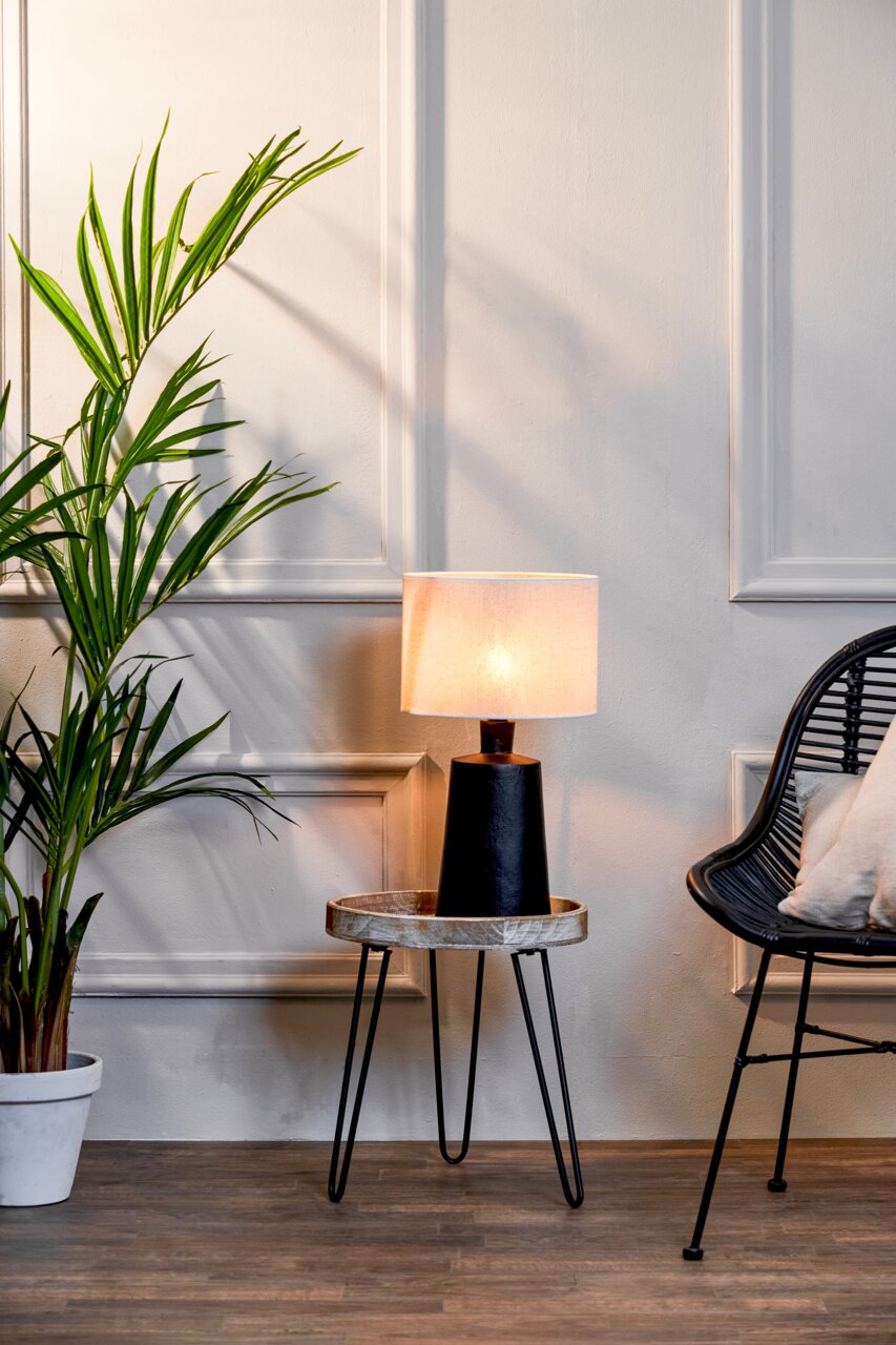 Moderner Lampenschirm auf einem kleinen Tisch, seitliche Perspektive, neben einer Pflanze und einem Stuhl.
