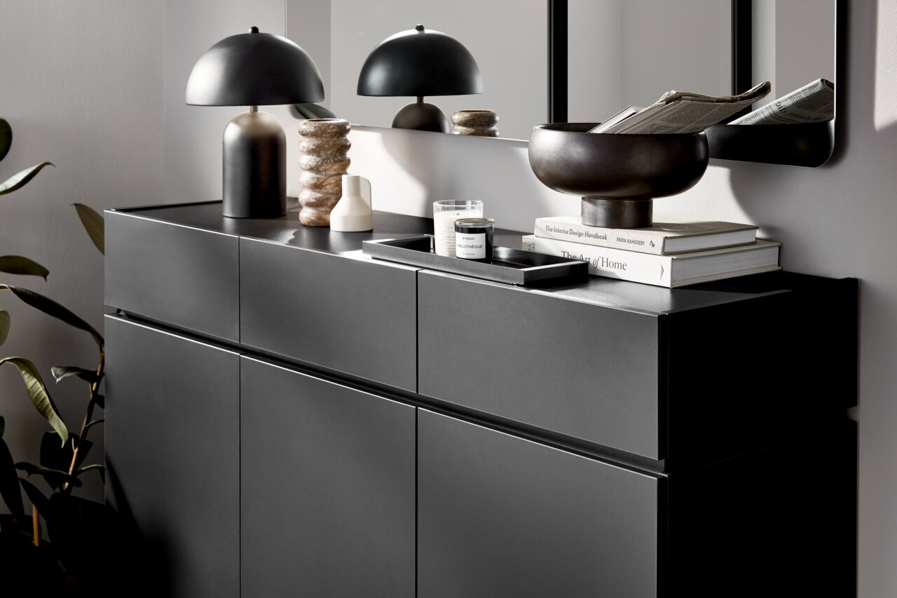 Moderner XL-Schuhschrank in dunklem Design, seitliche Perspektive, dekoriert mit Lampe, Büchern und Schale.