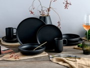 Mattschwarzes Geschirr-Set aus Keramik mit Tellern, Schalen und Bechern auf rustikalem Holztisch, dekoriert mit Vase und Beerenzweigen, in frontaler leicht seitlicher Perspektive