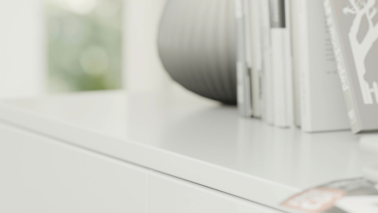 Nahaufnahme eines weißen Schuhschranks mit Büchern und einer Vase darauf, seitliche Perspektive.