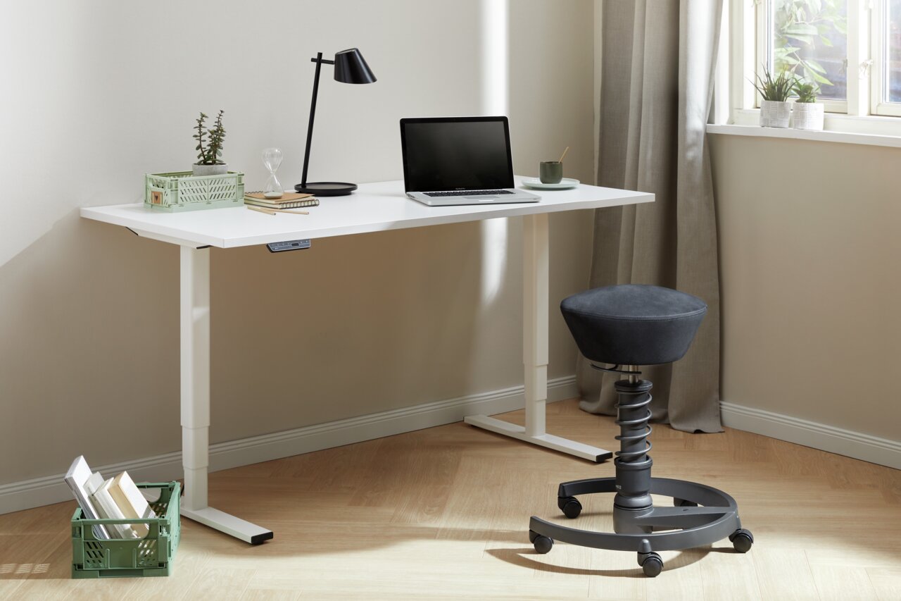 Moderner Sitzhocker mit ergonomischem Design und Rollen, seitliche Perspektive neben einem weißen Schreibtisch.