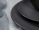 Nahaufnahme von zwei übereinander gestapelten, dunklen Tellern mit strukturierter Oberfläche, seitliche Perspektive.