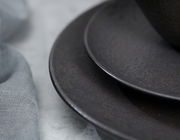 Nahaufnahme von zwei übereinander gestapelten, dunklen Tellern mit strukturierter Oberfläche, seitliche Perspektive.