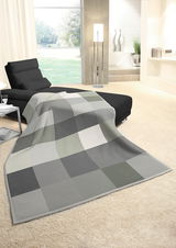 Gemütliche Wohndecke in Grau- und Grüntönen auf einem modernen Sofa in einem hellen Wohnzimmer mit Blick auf den Garten.