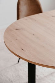 Nahaufnahme eines runden Esstisches aus hellem Holz mit schwarzem Metallgestell, seitliche Perspektive.