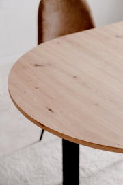 Nahaufnahme eines runden Esstisches aus hellem Holz mit schwarzem Metallgestell, seitliche Perspektive.