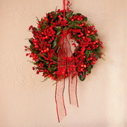 Weihnachtskranz mit roten Beeren und grünen Blättern, verziert mit einem roten Band, aus der Frontalperspektive fotografiert.
