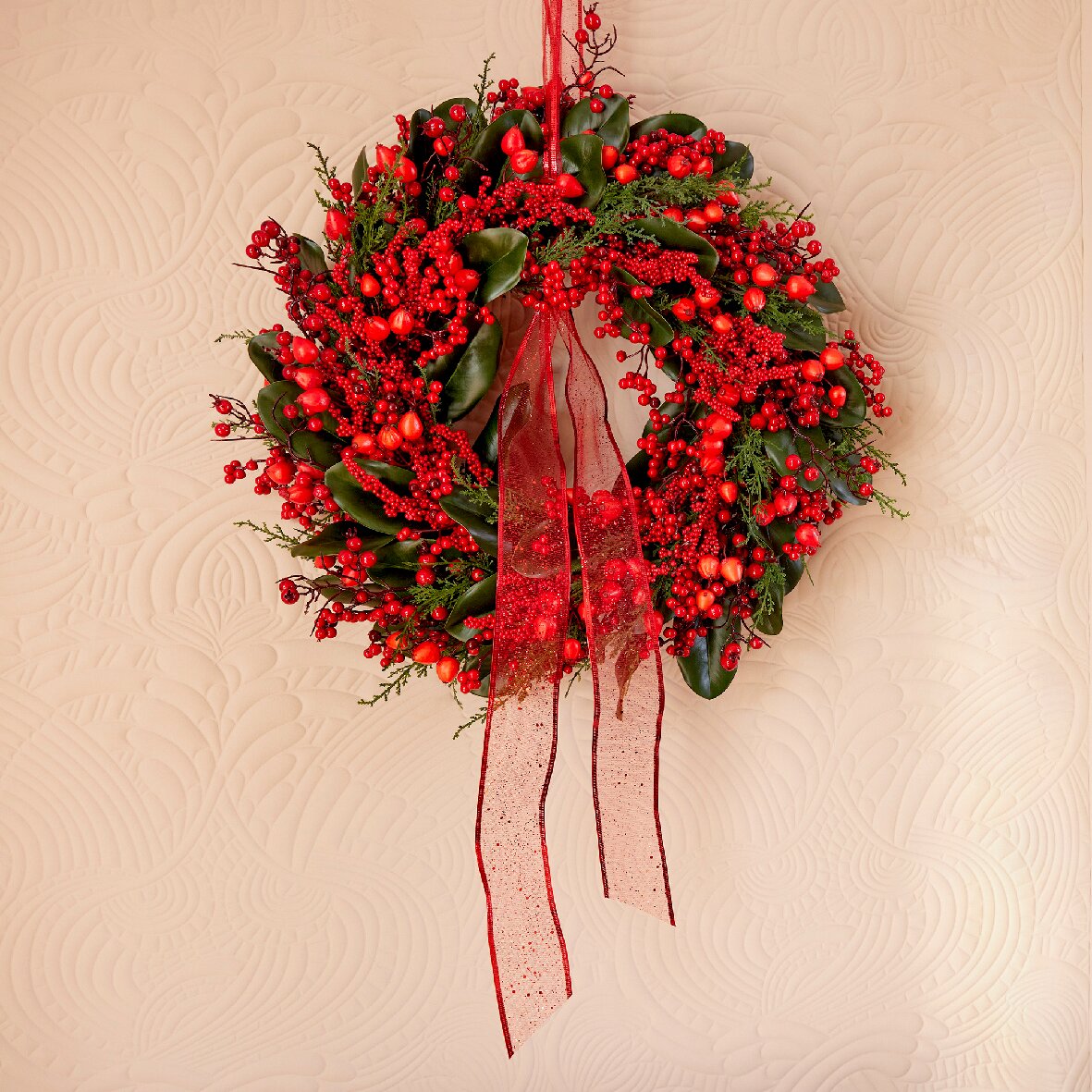 Weihnachtskranz mit roten Beeren und grünen Blättern, verziert mit einem roten Band, aus der Frontalperspektive fotografiert.