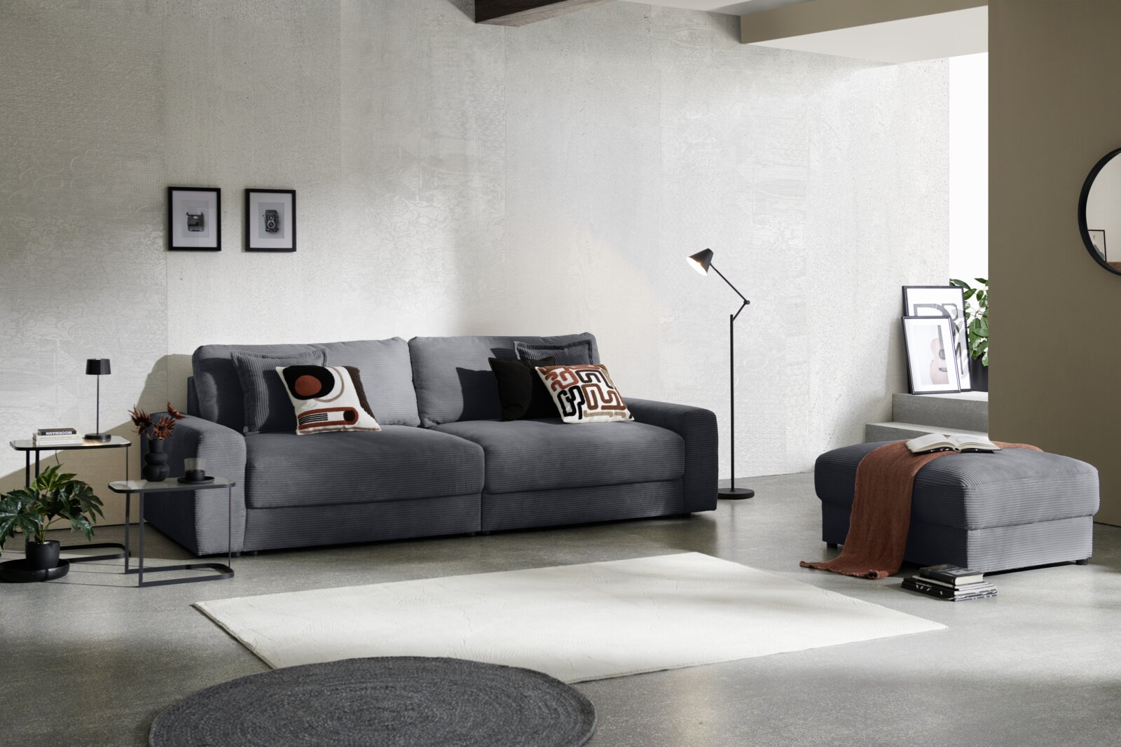 Z2 Grote bank NAPOLI Großes, graues Big-Sofa in modernem Wohnzimmer, seitliche Perspektive, mit dekorativen Kissen und passendem Hocker.