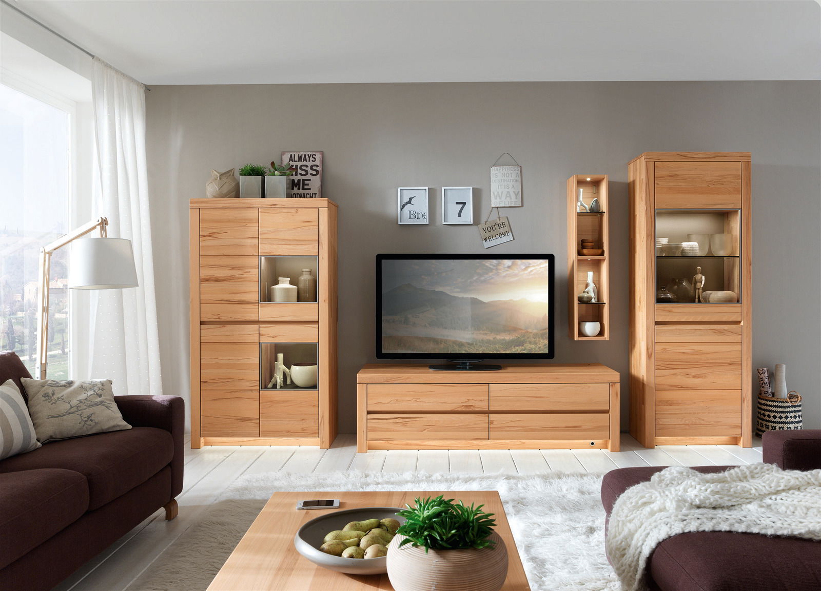 Wohnzimmeransicht mit Wöstmann Markenmöbel Wandkombination SOLEO 3000 in heller Holzoptik, bestehend aus zwei Vitrinen, einem TV-Board und einem Wandregal, frontal betrachtet.