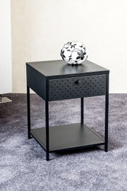 Schwarzer Nachttisch/Beistelltisch aus Metall mit Schublade (Lochmuster) und unterer Ablage, darauf eine weiße Vase mit schwarzem Blumenmuster, schräg von vorne fotografiert