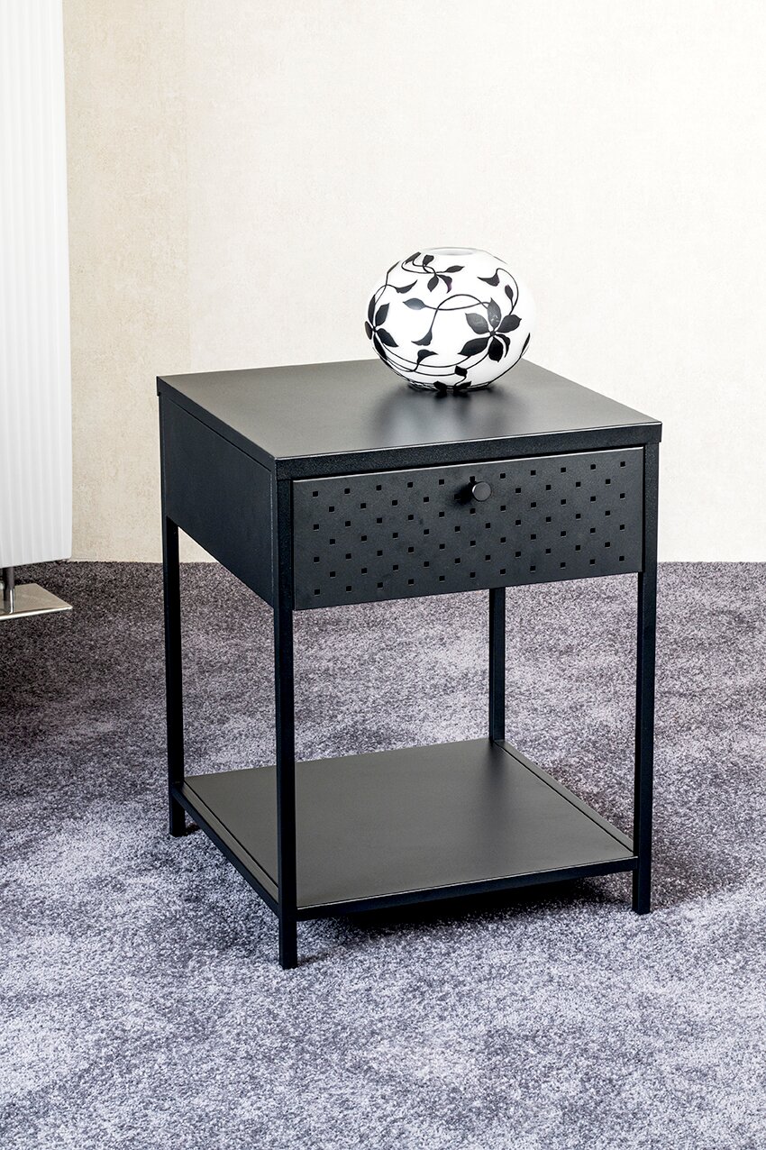Schwarzer Nachttisch/Beistelltisch aus Metall mit Schublade (Lochmuster) und unterer Ablage, darauf eine weiße Vase mit schwarzem Blumenmuster, schräg von vorne fotografiert