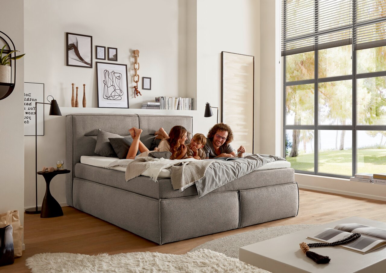 Gemütliches Boxspringbett in einem modernen Schlafzimmer, seitliche Perspektive, mit einer Familie, die darauf entspannt.