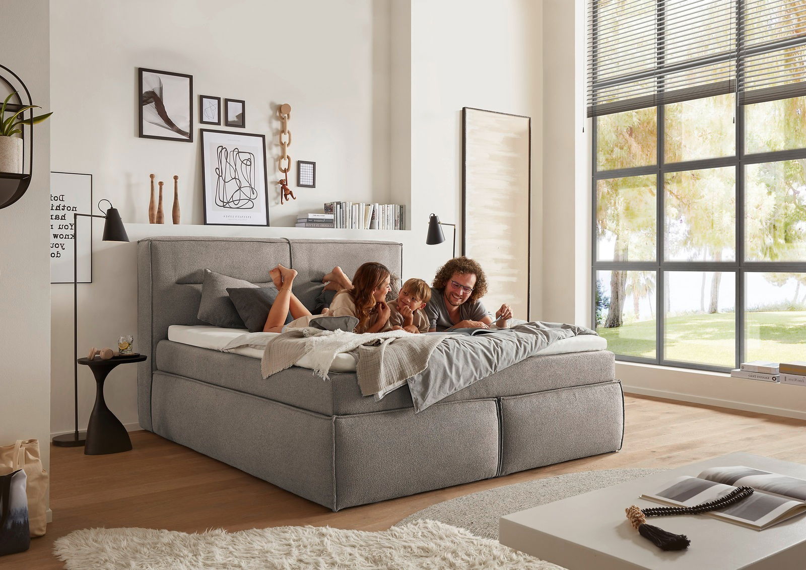 Gemütliches Boxspringbett in einem modernen Schlafzimmer, seitliche Perspektive, mit einer Familie, die darauf entspannt.