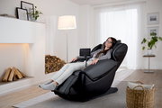 Frau entspannt in einem modernen schwarzen Massagesessel in einem gemütlichen Wohnzimmer, seitliche Perspektive