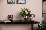Drei klare Glasvasen auf einem Regal, eine mit Blumenarrangement, die anderen mit Kerzen, aus seitlicher Perspektive.