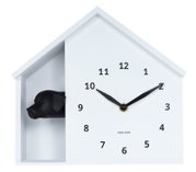Weiße Wanduhr in Hausform mit schwarzem Hundekopf, frontal betrachtet.