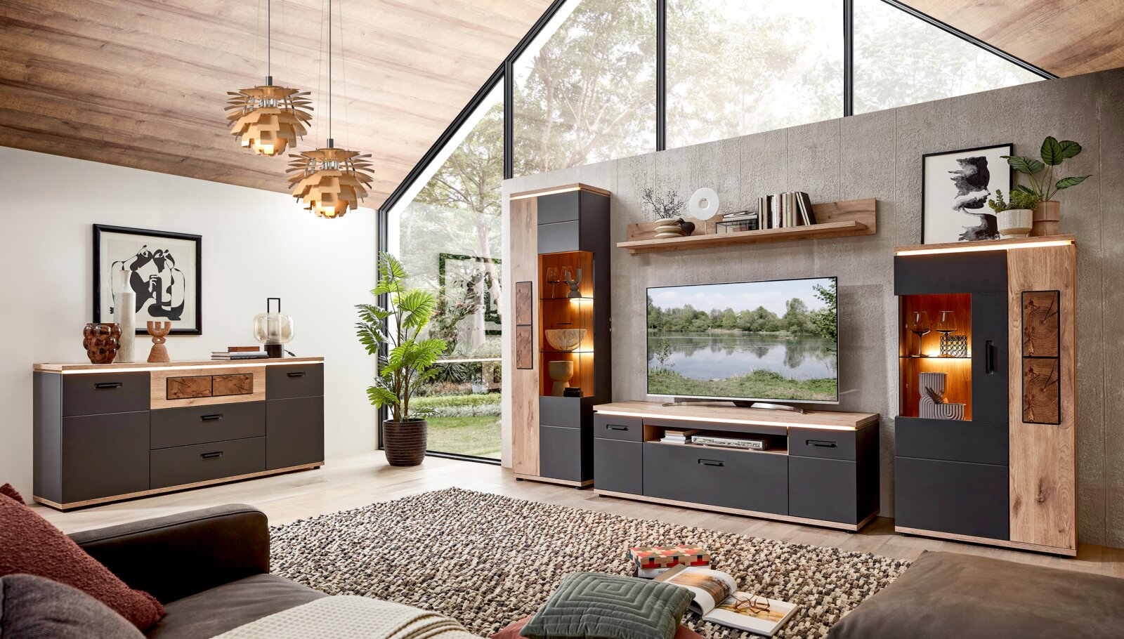Modernes Wohnzimmer-Set in Holzoptik und Anthrazit mit Sideboard, TV-Lowboard, zwei Vitrinen mit Beleuchtung und Wandregal, frontal aus leicht schräger Perspektive fotografiert.