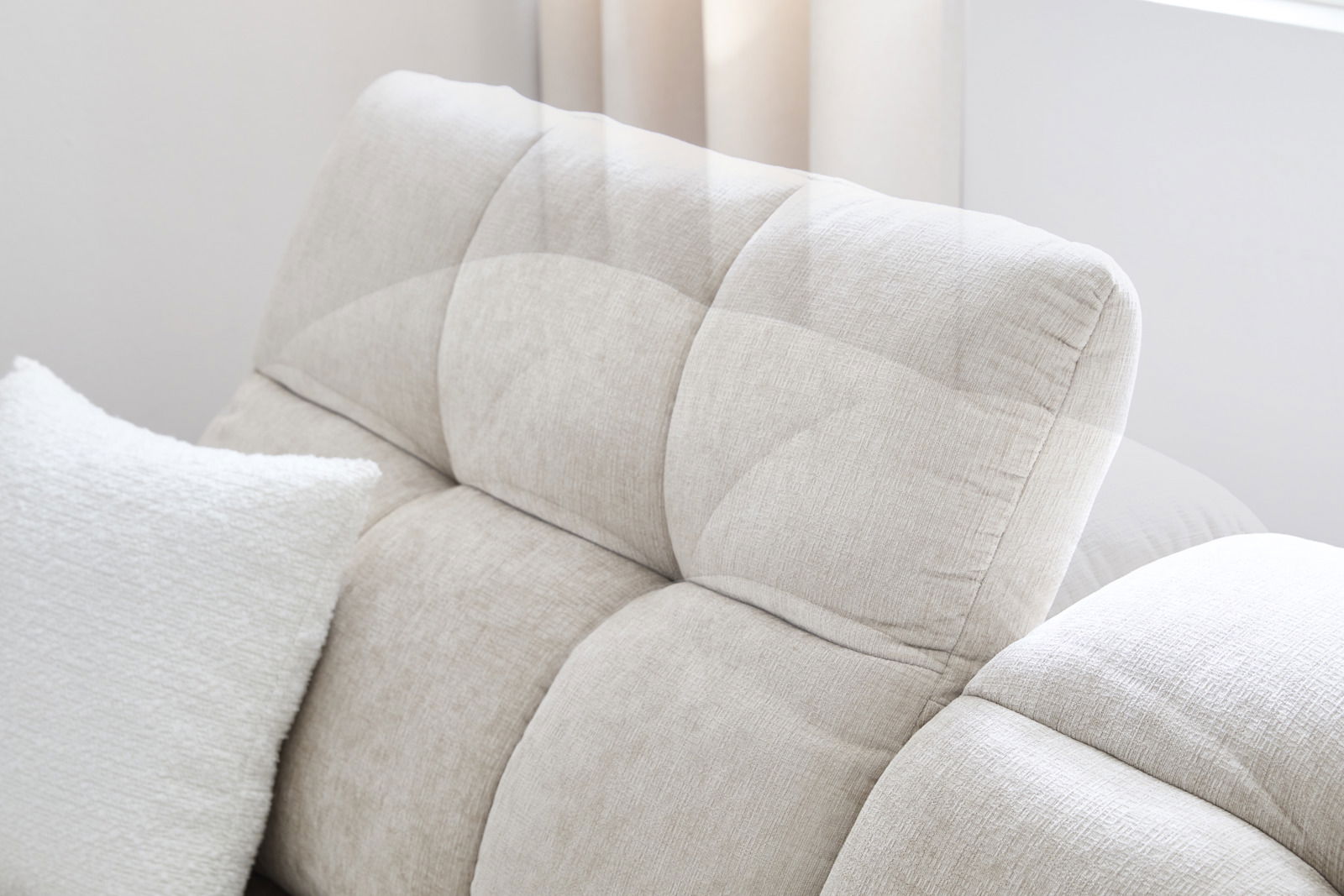 Nahaufnahme eines beigen Sofas mit gepolsterter Rückenlehne und einem weißen Kissen, seitliche Perspektive
