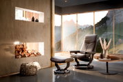 Moderne fauteuil met bijpassende voetenbank in een stijlvolle ruimte met panoramische ramen en uitzicht op de bergen, zijaanzicht.