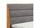 Nahaufnahme eines Boxspringbettes mit grauem, gepolstertem Kopfteil und Holzrahmen, seitliche Perspektive