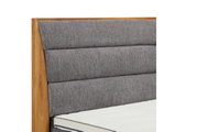 Close-up van een boxspringbed met een grijs, gestoffeerd hoofdeinde en een houten frame, gezien vanaf de zijkant
