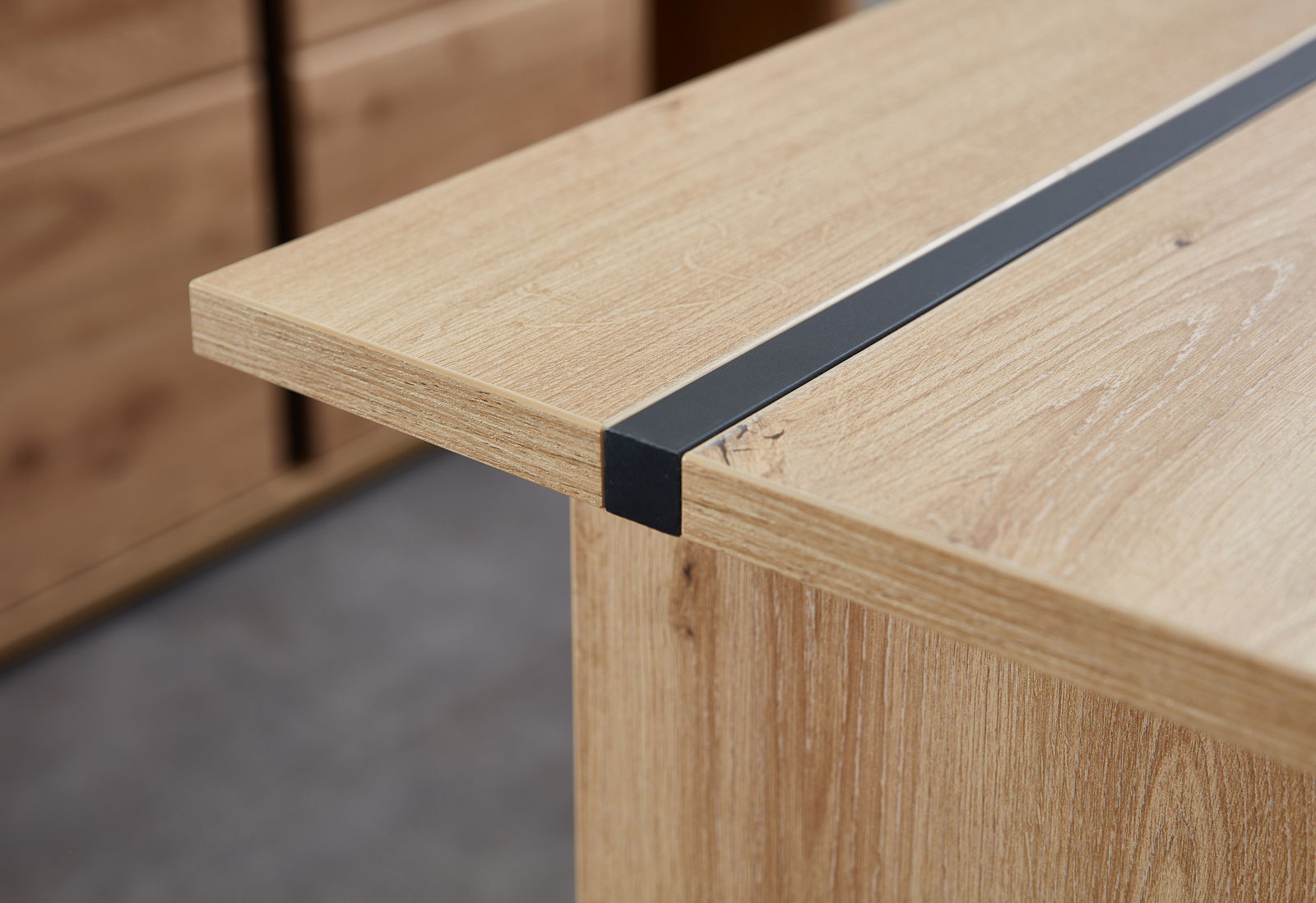 Nahaufnahme eines Schreibtisches aus Holz mit einer schwarzen Metallleiste, seitliche Perspektive.