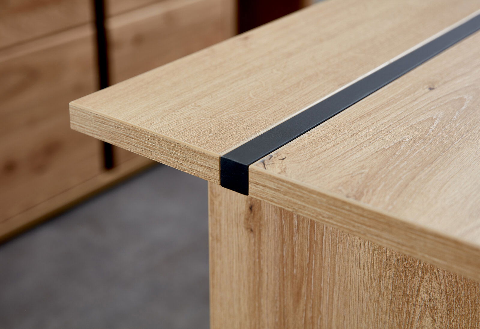 Nahaufnahme eines Schreibtisches aus Holz mit einer schwarzen Metallleiste, seitliche Perspektive.