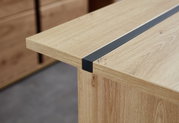Nahaufnahme eines Schreibtisches aus Holz mit einer schwarzen Metallleiste, seitliche Perspektive.