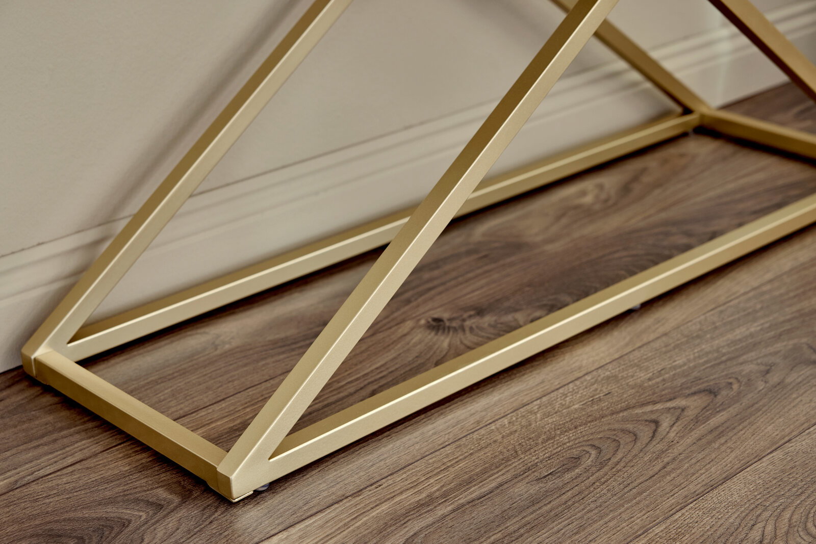 Nahaufnahme der goldenen Metallstruktur einer Konsole auf einem Holzboden, seitliche Perspektive.