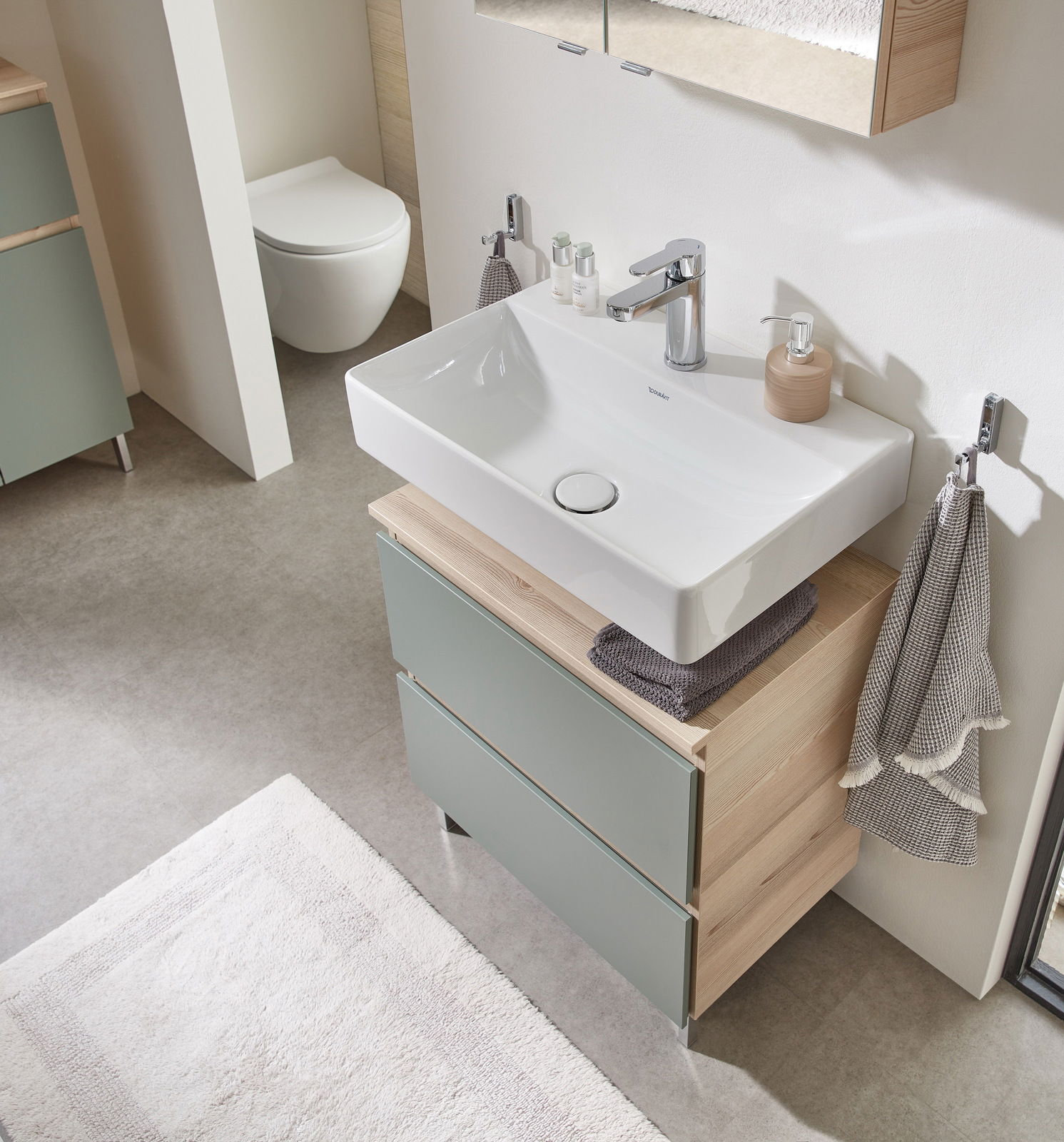 Moderner Waschbeckenunterschrank mit zwei Schubladen in Holzoptik und grünlichen Fronten, von oben fotografiert.