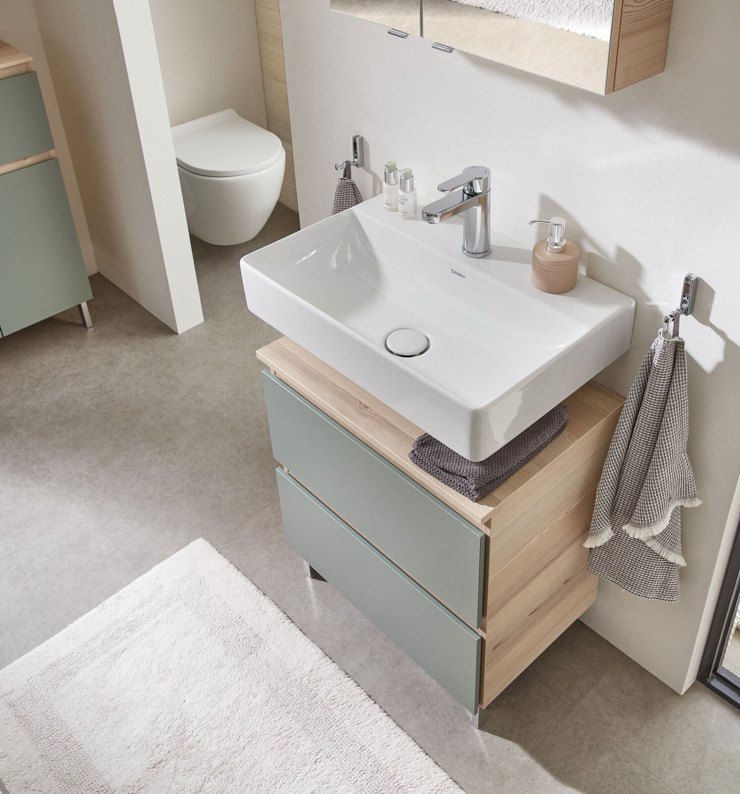 Moderner Waschbeckenunterschrank mit zwei Schubladen in Holzoptik und grünlichen Fronten, von oben fotografiert.