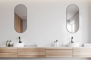 Zwei ovale Spiegel, ca. 30x70 cm, über einem modernen Doppelwaschbecken mit Holzunterschrank, aus der Frontalperspektive.