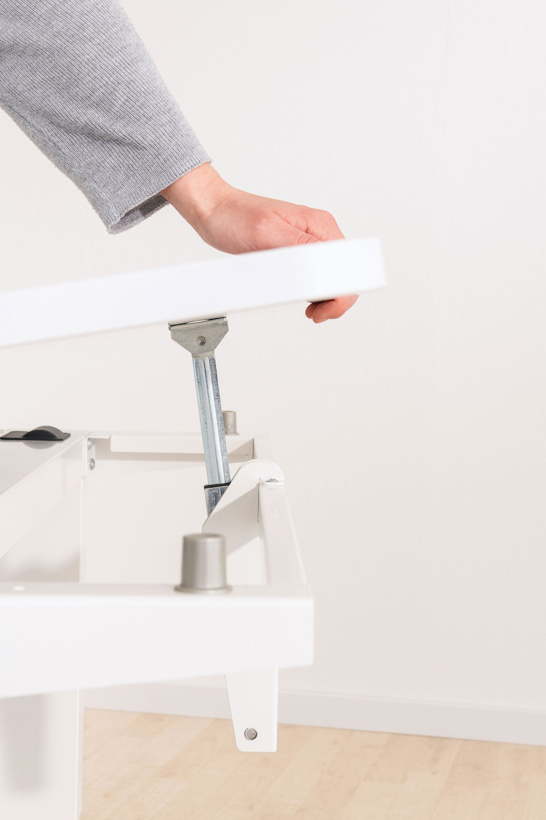 Nahaufnahme eines weißen Schreibtischs mit verstellbarer Tischplatte, die von einer Hand angehoben wird. Perspektive von der Seite.