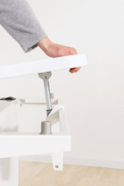 Close-up van een wit bureau met een verstelbaar tafelblad dat door een hand omhoog wordt getild. Zijaanzicht.