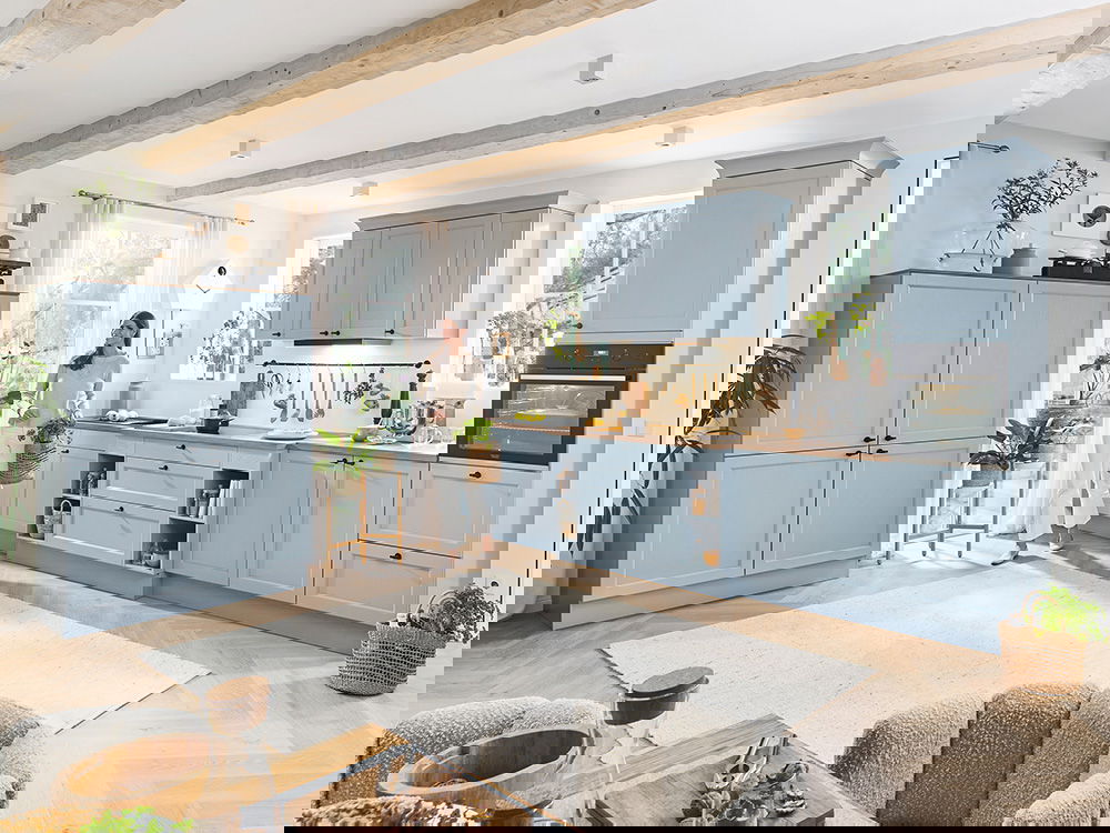 Helle Landhausküche in Pastellblau mit Holzdetails, gemütlicher Atmosphäre und viel natürlichem Licht.