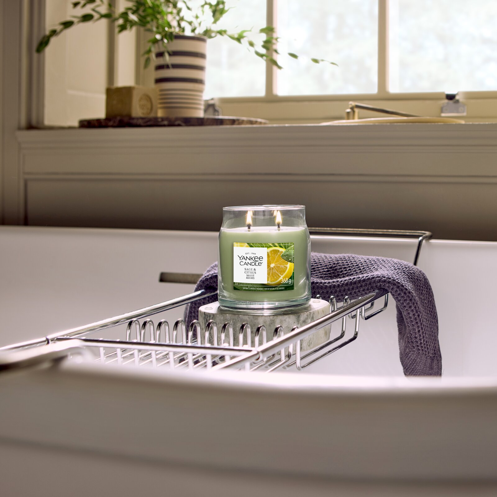 Yankee Candle Sage & Citrus Duftkerze mit zwei brennenden Dochten im Glas, frontal in stimmungsvoller Badezimmerkulisse auf einer Badewannenablage präsentiert