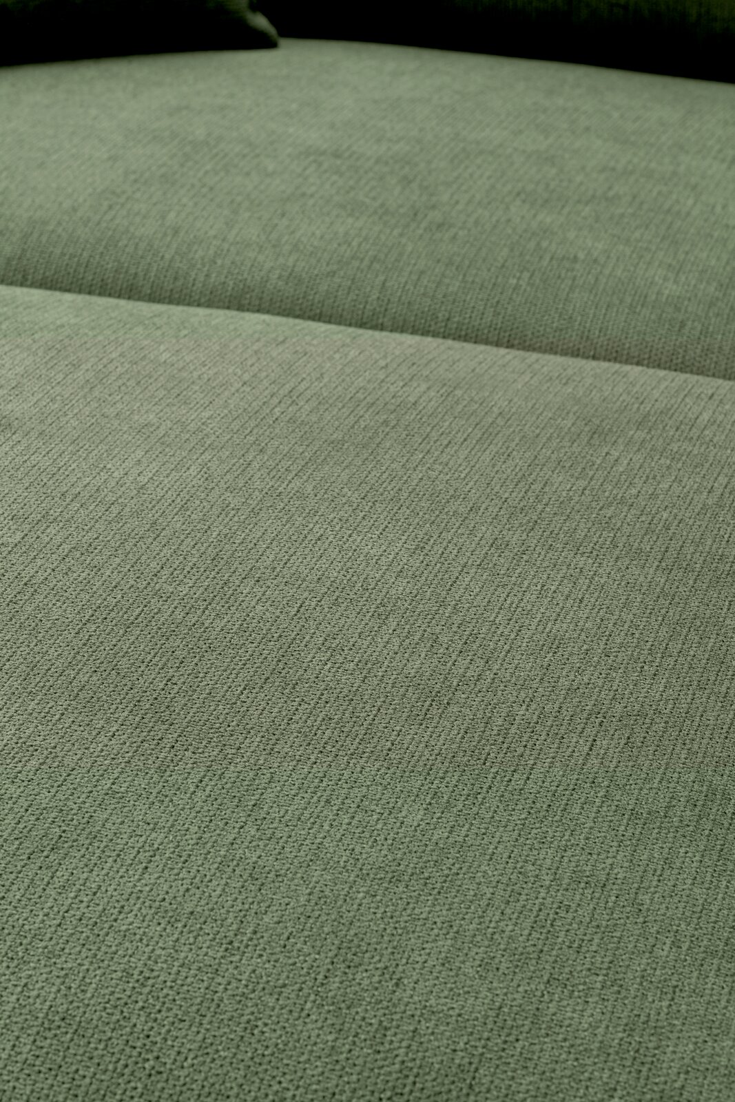 Nahaufnahme der grün melierten Stoffpolsterung eines Sofas mit sichtbarer Sitz- und Rückenfläche, fotografiert aus leicht schräger Draufsicht.