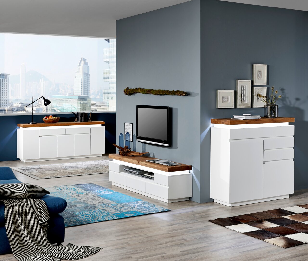 Moderne Wohnzimmermöbel in Weiß mit Holzoberflächen, darunter ein TV-Lowboard, ein Sideboard und eine Kommode, aus der Perspektive eines offenen Wohnbereichs mit Blick auf die Stadt.