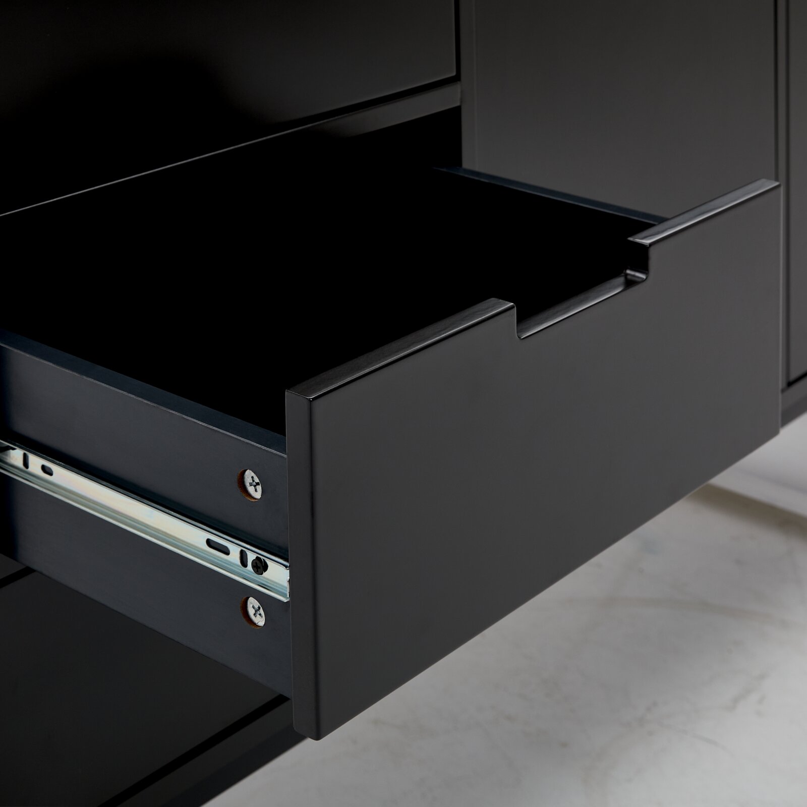 Nahaufnahme einer geöffneten Schublade eines schwarzen Sideboards, seitliche Perspektive