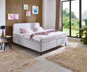 Modernes Boxspringbett in einem stilvollen Schlafzimmer mit Holzwandverkleidung und großen Fenstern, seitliche Perspektive.