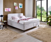 Modern boxspringbed in een stijlvolle slaapkamer met houten lambrisering en grote ramen, zijaanzicht.