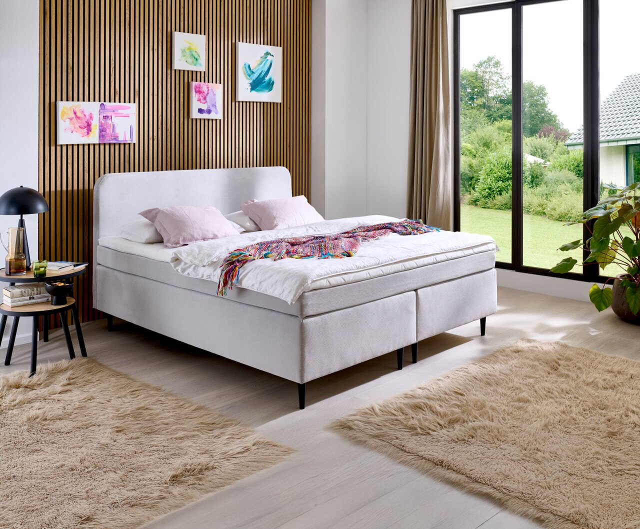 Modern boxspringbed in een stijlvolle slaapkamer met houten lambrisering en grote ramen, zijaanzicht.