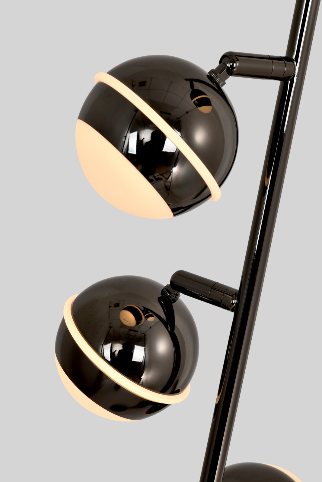 Detailaanzicht vanuit schuin vooraanzicht van een moderne zwarte vloerlamp met glanzende bolvormige kappen en warmwit licht.