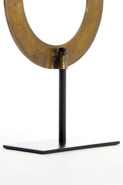 Nahaufnahme eines metallischen Ornaments in Ringform auf einem schwarzen Ständer, seitliche Perspektive.
