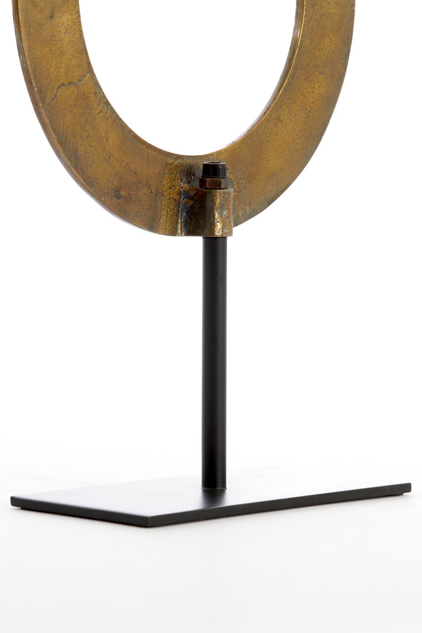Nahaufnahme eines metallischen Ornaments in Ringform auf einem schwarzen Ständer, seitliche Perspektive.
