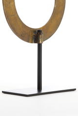 Nahaufnahme eines metallischen Ornaments in Ringform auf einem schwarzen Ständer, seitliche Perspektive.