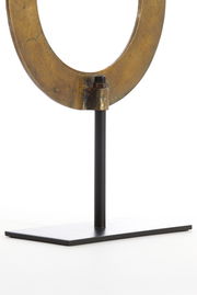 Nahaufnahme eines metallischen Ornaments in Ringform auf einem schwarzen Ständer, seitliche Perspektive.
