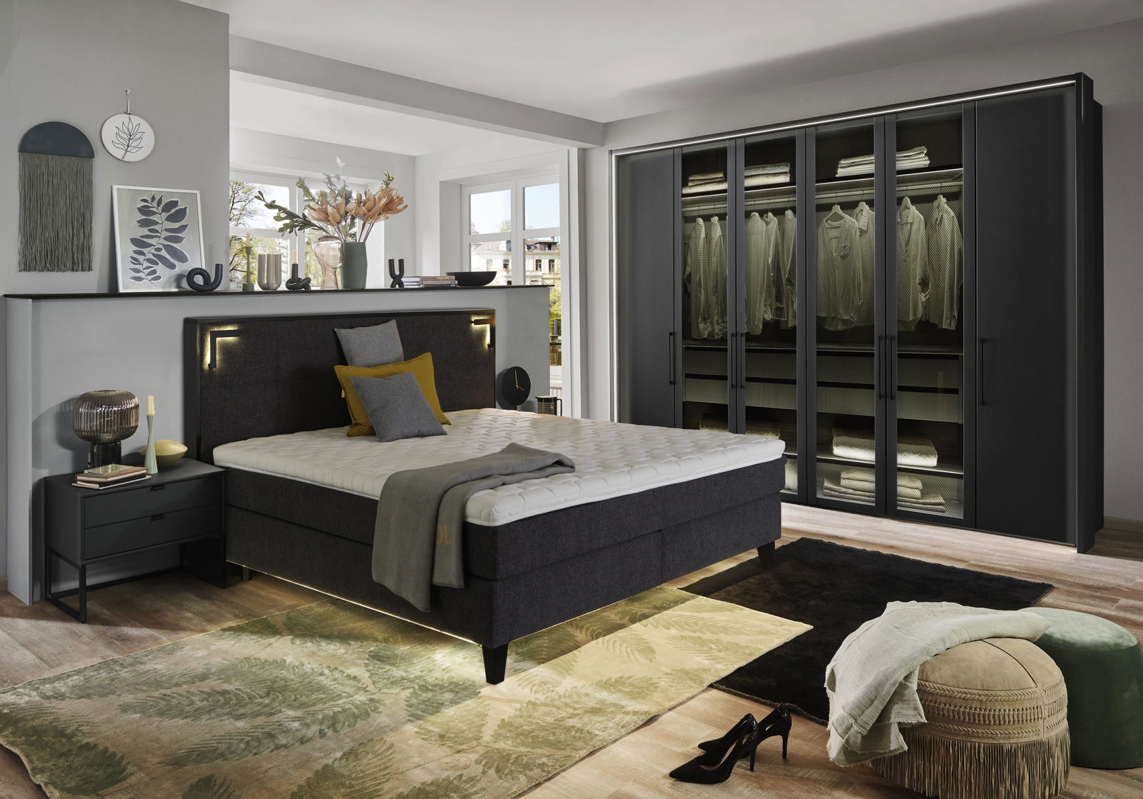 Moderne Schlafzimmeransicht mit einem großen, sechstürigen Drehtürenschrank in dunklem Design, neben einem stilvollen Bett mit gepolstertem Kopfteil. Perspektive von der Seite des Bettes.